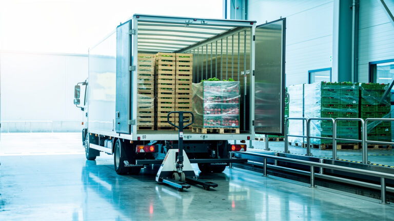 Camion frigorifique blanc à quai chargeant des palettes de produits frais dans un entrepôt alimentaire propre et moderne.