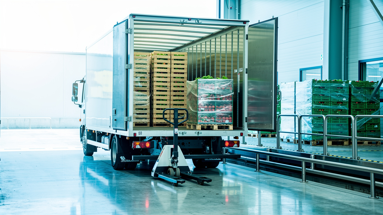 Camion frigorifique blanc à quai chargeant des palettes de produits frais dans un entrepôt alimentaire propre et moderne.